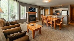 Una sala de estar con chimenea, televisor y comedor con mobiliario de madera.