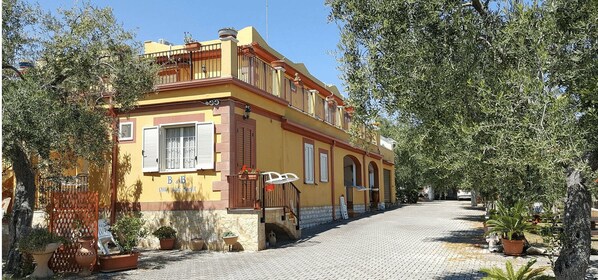 Une villa jaune dotée d’un balcon, d’une cour dallée et de plantes en pot.