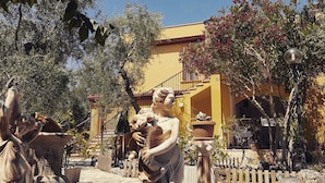 A courtyard with classical statues, a yellow building, and a wooden fence. - Villa Vale Mery (Vieste)