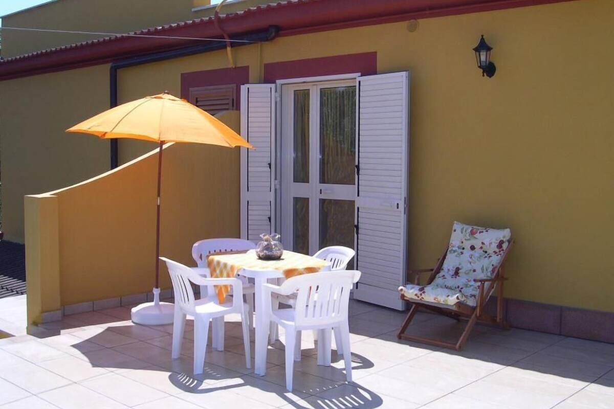 An outdoor patio with a table and chairs, a wooden chair, and a yellow umbrella.
