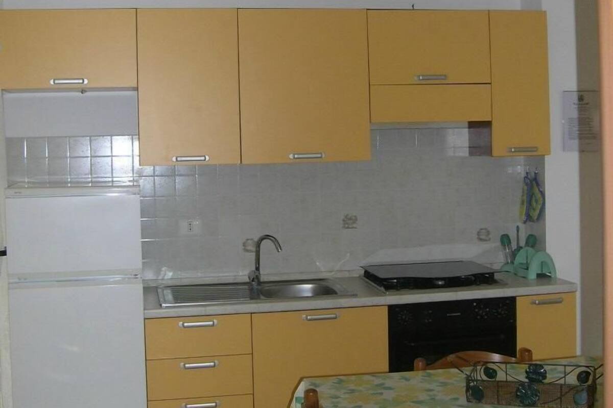 A compact kitchen with yellow cabinets, a white refrigerator, a sink, and a dining table with a floral tablecloth.