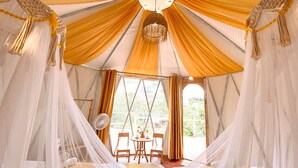 Una carpa con cama, mesa, sillas y ventilador.