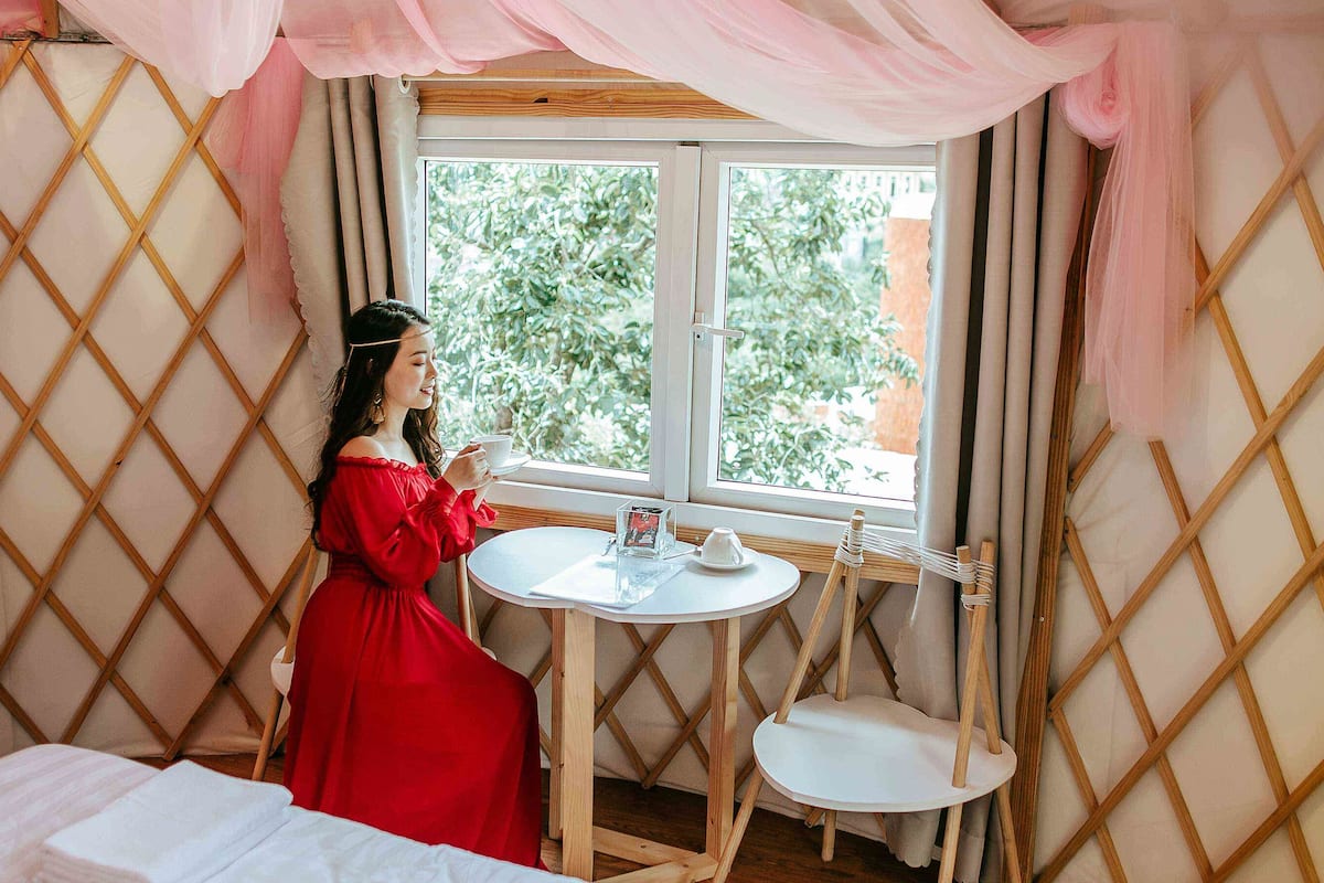 Ein Zimmer mit einem Holzgitter, einem kleinen runden Tisch mit Tasse und Untertasse sowie einem Fenster mit Vorhängen.