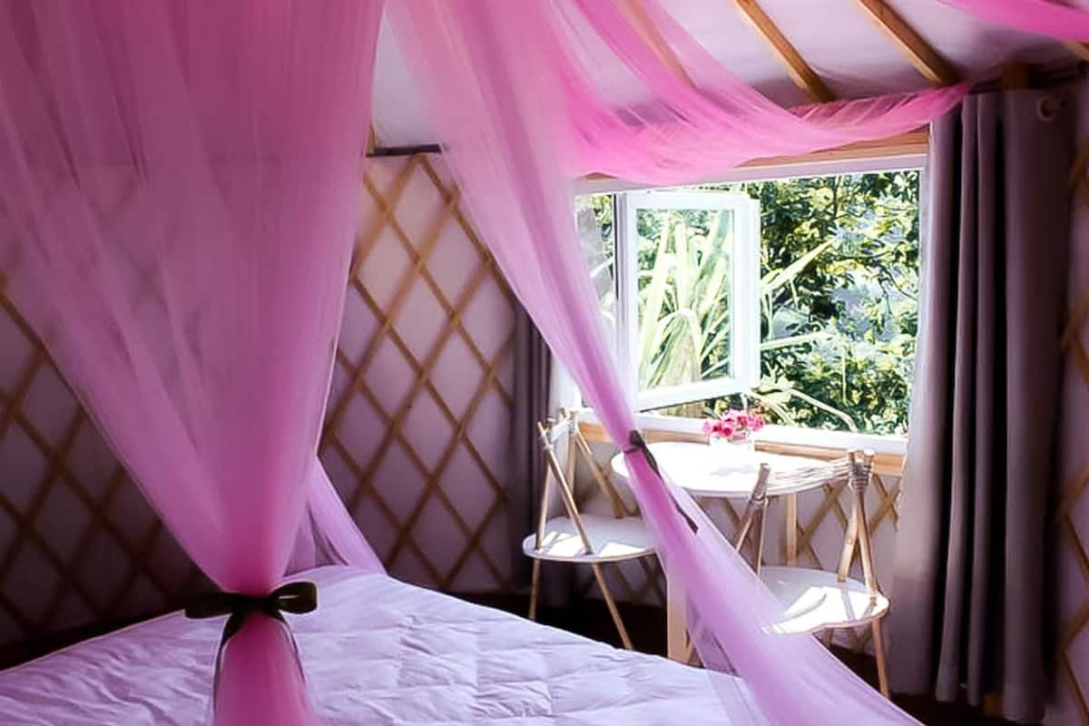 Ein Schlafzimmer mit Baldachinbett, einem kleinen Tisch mit Stühlen und einem Fenster mit Blick ins Grüne.
