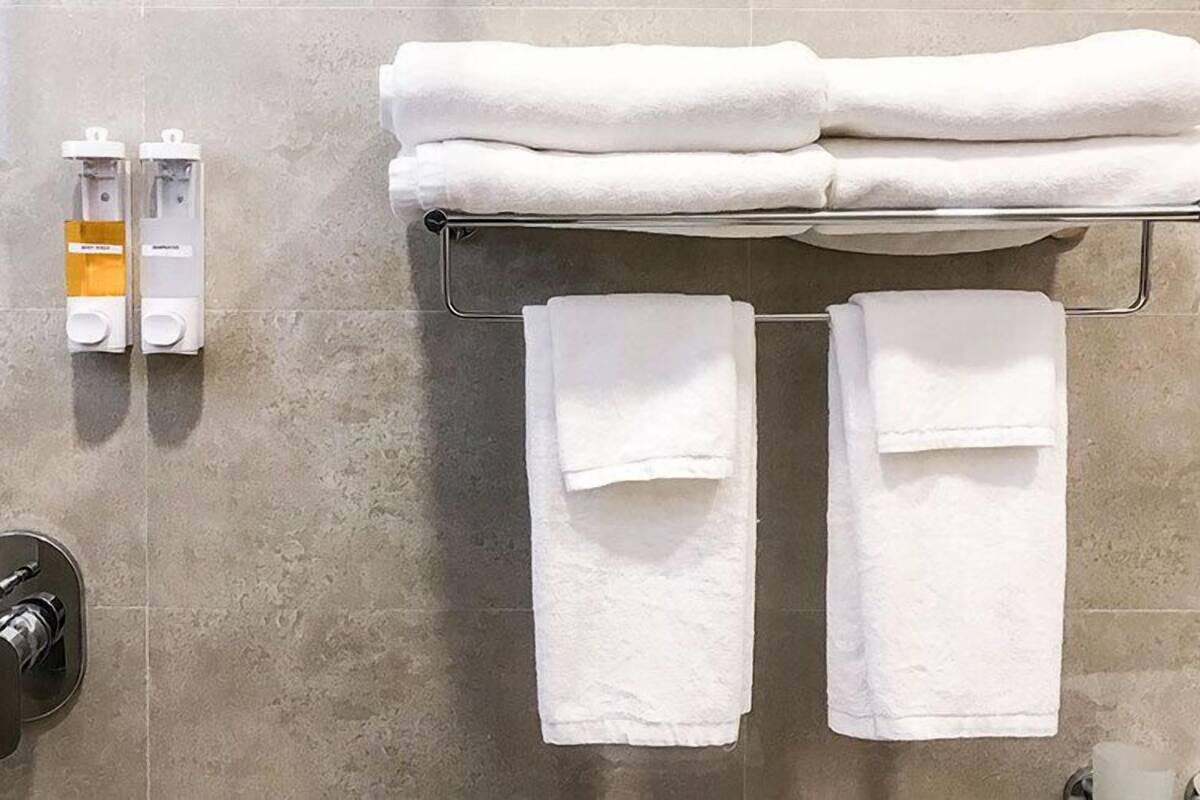 A bathroom with a towel rack holding three folded towels, a hand dryer, and a paper towel dispenser.