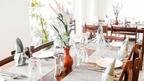 A dining area with wooden tables set for a meal, featuring clear glassware and a central floral arrangement. - Hotel Dralha (Thimphu)