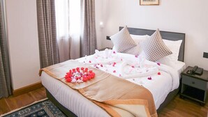 A neatly made bed with white linens, a floral arrangement, and checkered pillows. - Hotel Dralha (Thimphu)