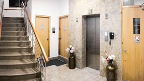 A hotel lobby with a staircase, two wooden doors, an elevator, and two vases with flowers. - Hotel Dralha (Thimphu)