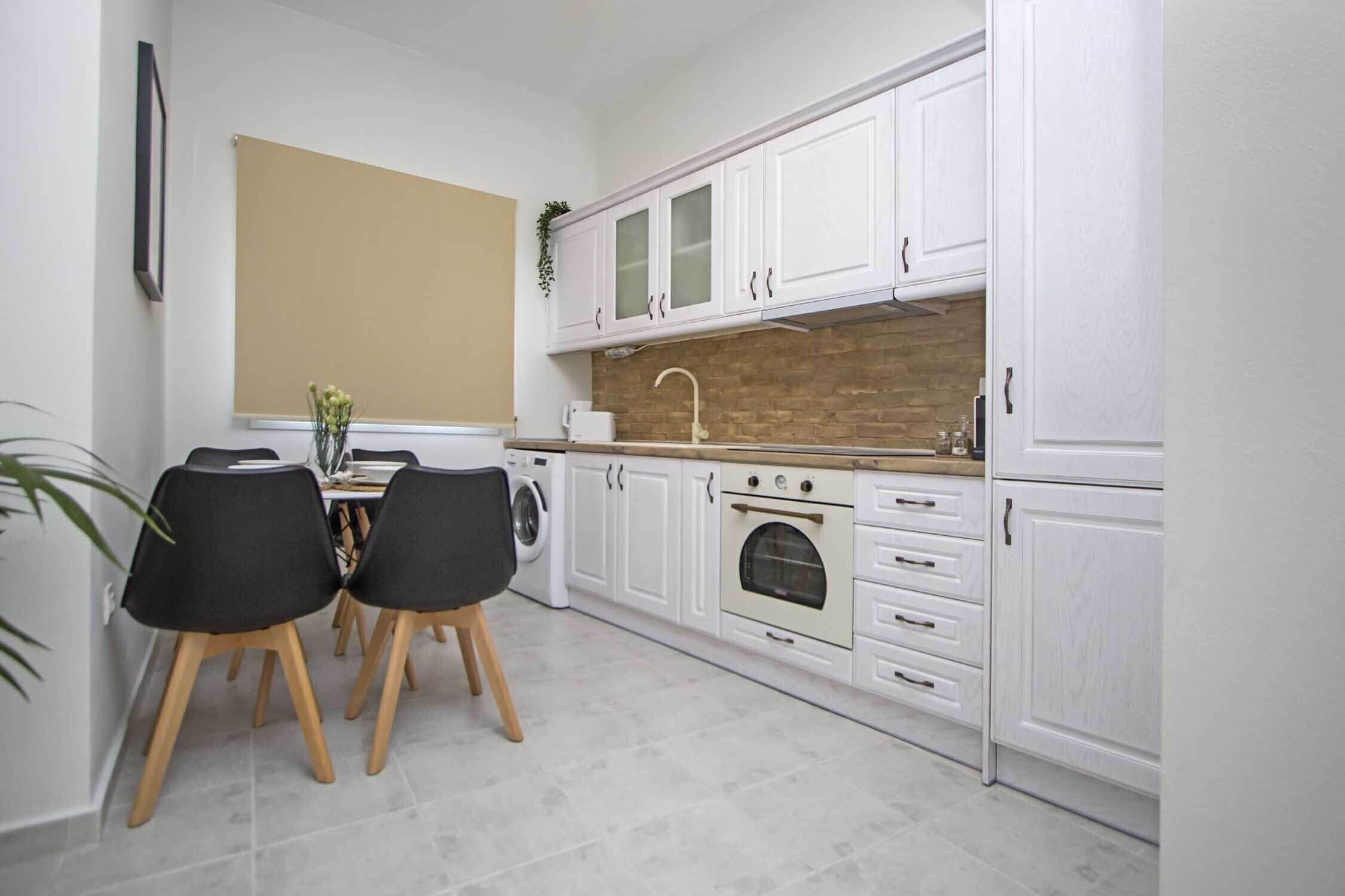Una cocina compacta con armarios blancos, horno empotrado y una zona de comedor con dos sillas.