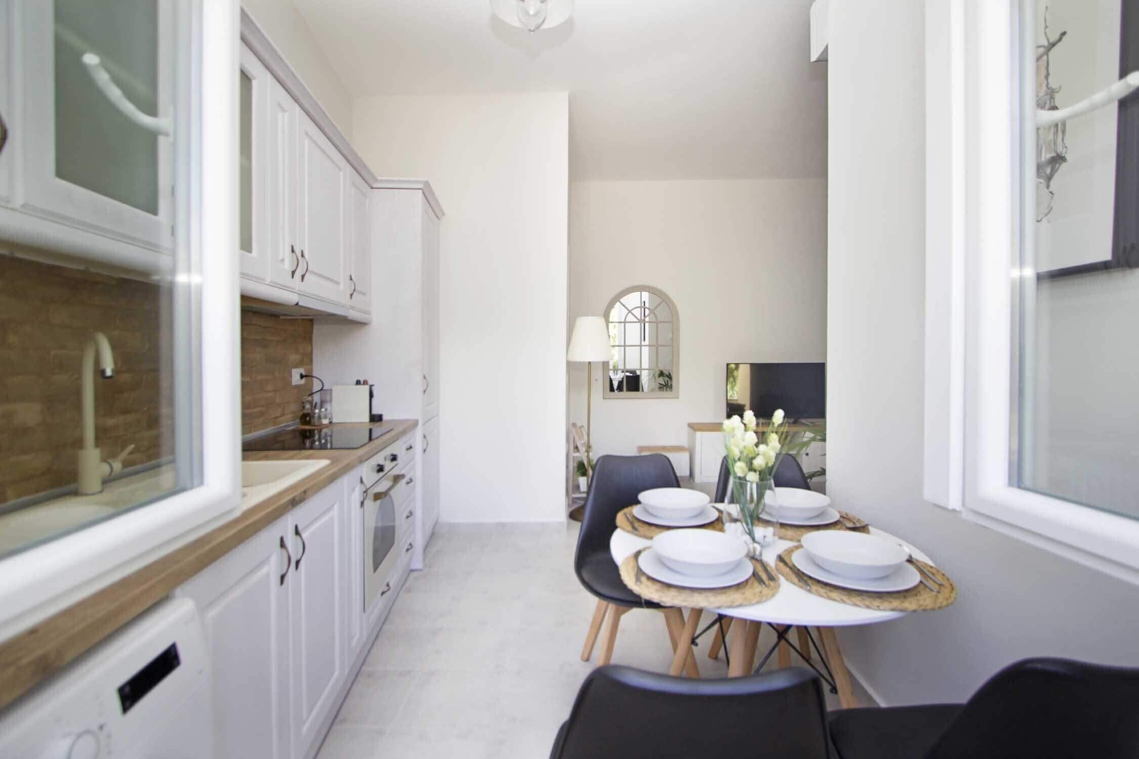 A modern kitchen with white cabinets, a wooden countertop, and a dining area with a round table set for four.