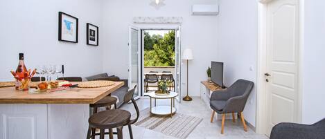 A modern kitchen with a dining area, a bar stool, a table with a vase, and a TV.