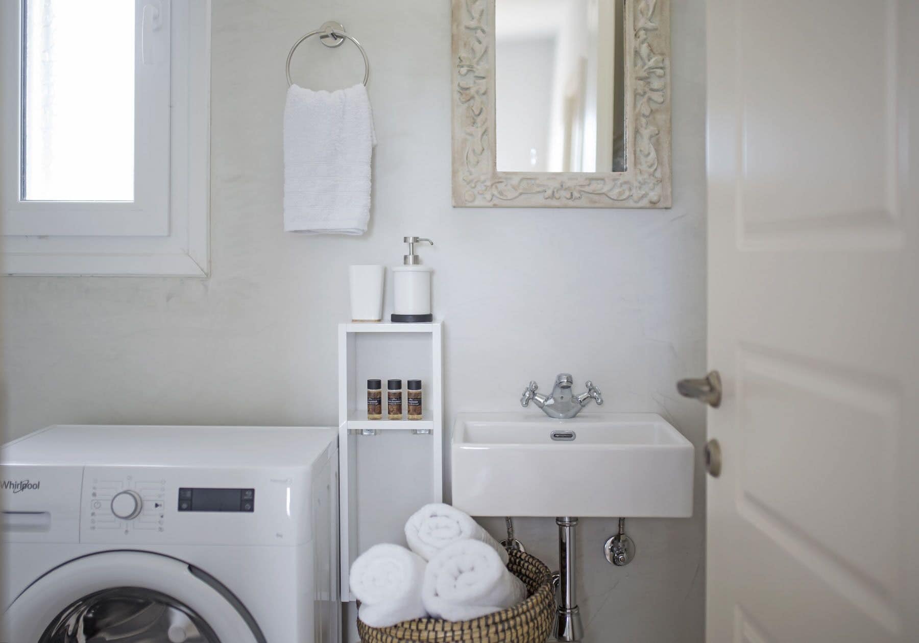 A compact bathroom with a washing machine, a sink, and a mirror.