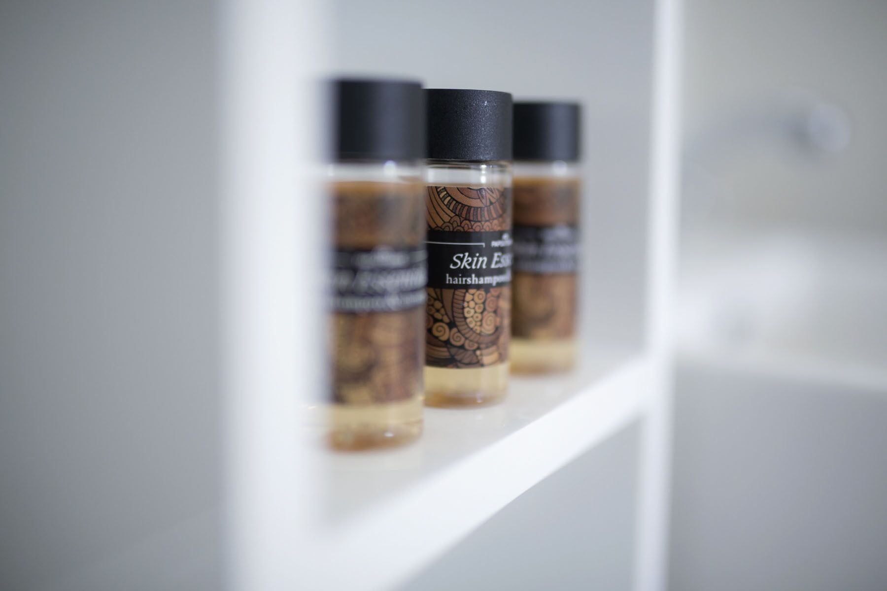 Drei Flaschen Skin Essence Haarschampoo auf einem weißen Regal.