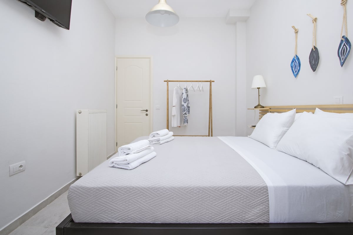 A neatly made bed with white linens, a wooden headboard, a bedside table with a lamp, and a wall-mounted TV.