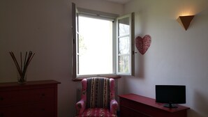 Una habitación con ventana, una silla, un aparador, un televisor y una decoración con forma de corazón en la pared.