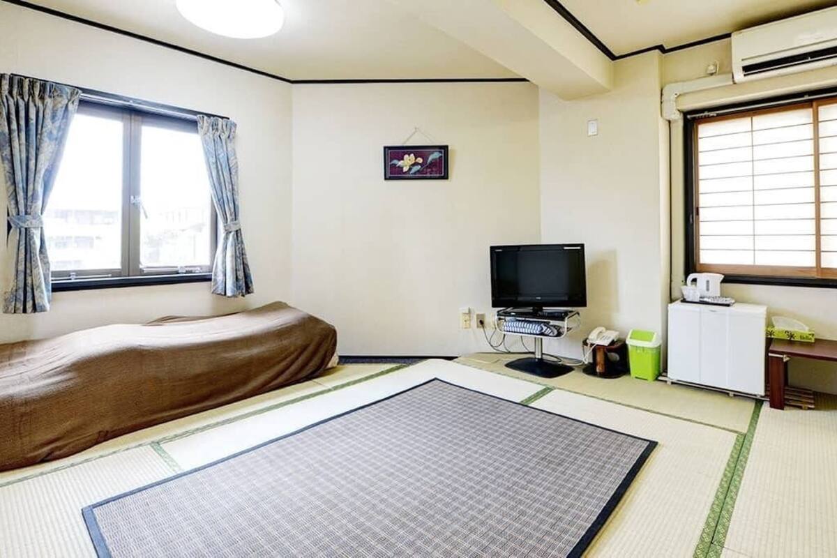 A room with a bed, a television, a small table, and a window with curtains.