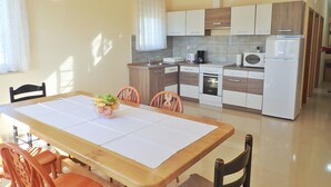 A compact kitchen with modern appliances, a dining area with a wooden table and chairs, and a bright, sunlit room.