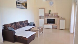 A living room with a sofa, coffee table, TV, and a small refrigerator.