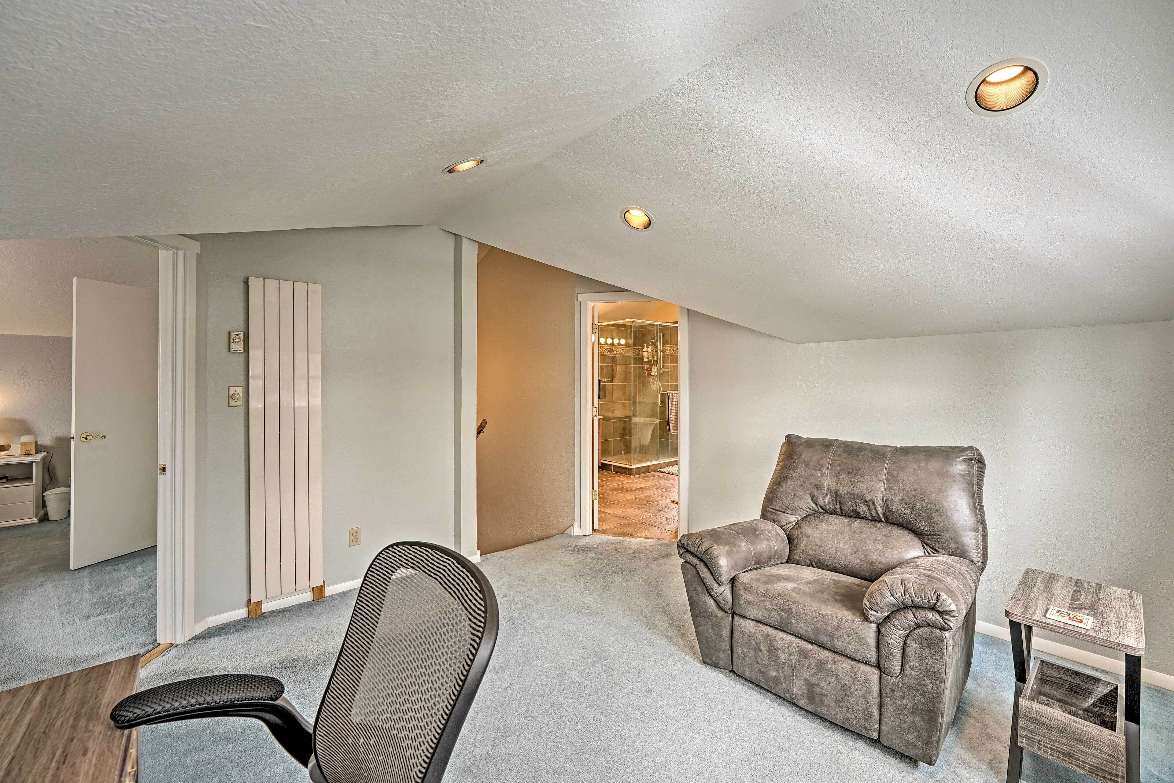 A spacious living area with a leather armchair, a small side table, and a door leading to a bathroom.