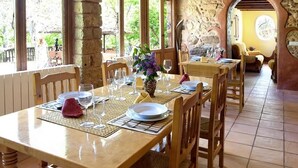 A dining area with wooden tables and chairs, stone walls, and large windows. - Country House La Posada Del Río Carbo. (Villahermosa del Río, España –)