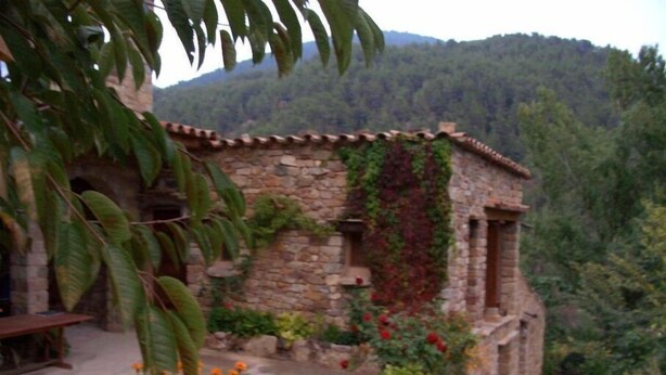 A stone building with a tiled roof, surrounded by greenery and flowering plants. - Country House La Posada Del Río Carbo. (Villahermosa del Río, España –)