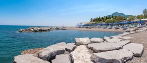 Ein Strand mit felsigem Ufer, einer Mole und einer Reihe von Strandsonnenschirmen.