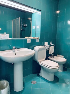 Ein Badezimmer mit blaustichigen Fliesen, einem Waschbecken, einer Toilette und einem Bidet.