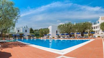 Ein Pool mit Liegestühlen und Sonnenschirmen, umgeben von Bäumen und weißen Gebäuden.