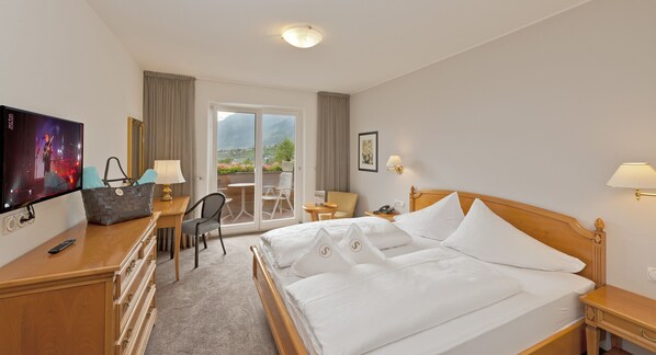 A hotel room with a bed, a desk with a TV, a chair, a table, and a view of the outdoors. - Hotel Restaurant Schennerhof (Merano)