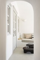 Un pasillo estrecho con puertas blancas, un banco con cojines y una pequeña mesa con una lámpara y libros.