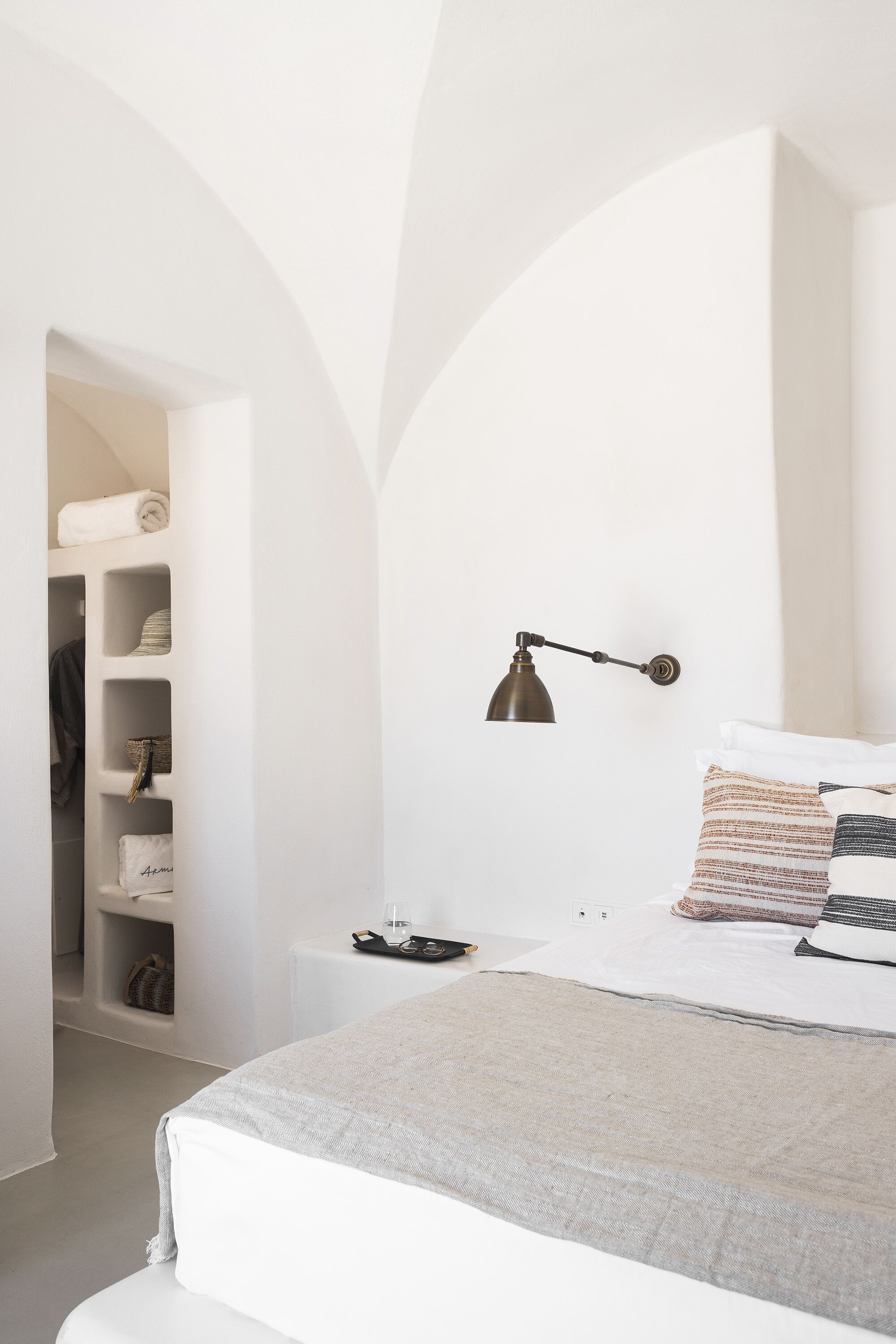 A minimalist bedroom with a bed, a bedside lamp, and a built-in wardrobe.