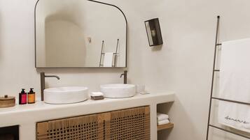Een badkamer met een rond wastafel, een spiegel, een handdoekhouder en een klein plankje met toiletartikelen.