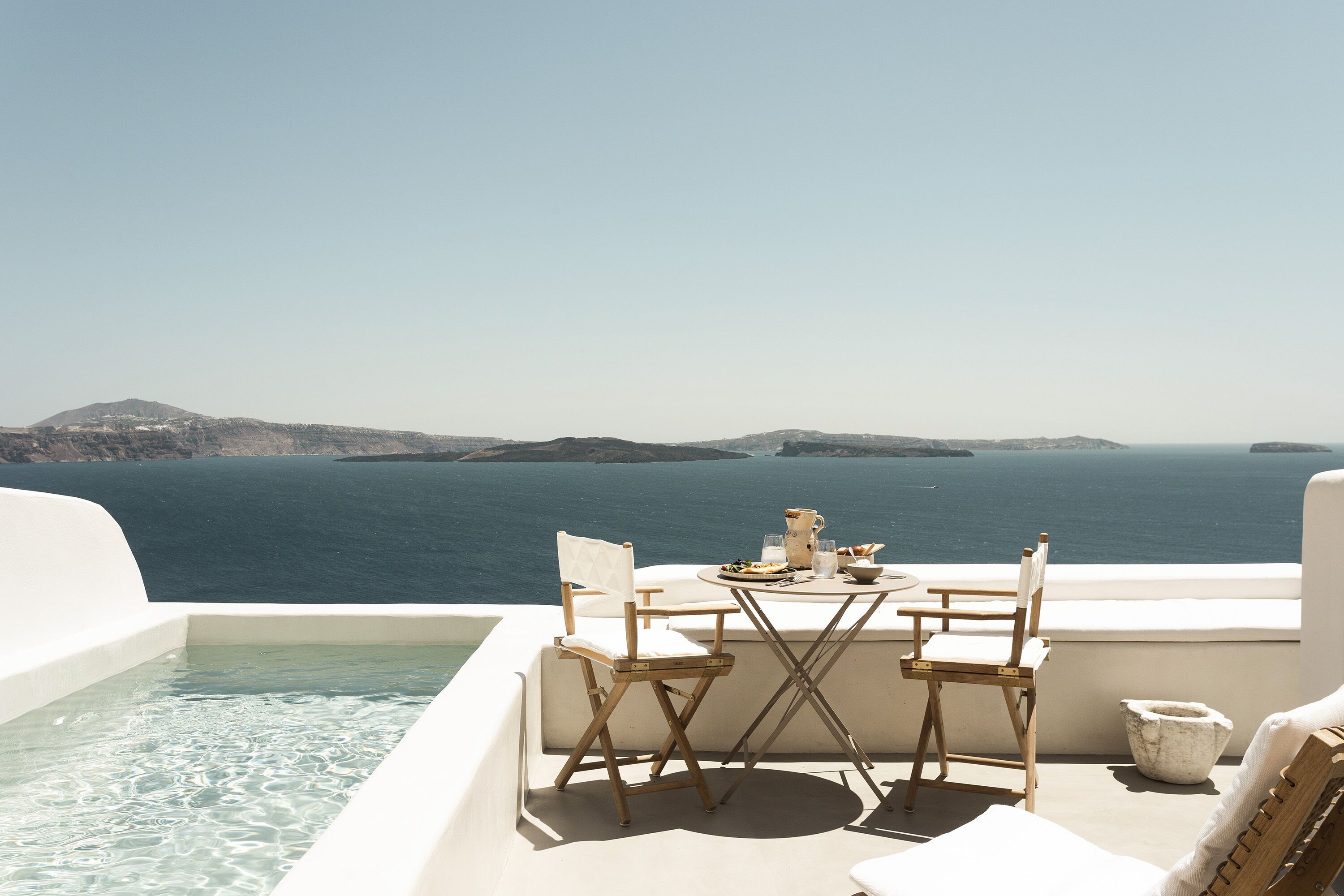 A terrace with a table and chairs overlooking a body of water and distant land.