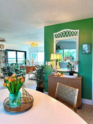 Uma área de refeições com uma mesa branca, um vaso de flores e um espelho sobre um console de madeira.