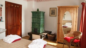 Une pièce avec une armoire en bois, une chaise en osier avec un coussin rouge, un lit avec une literie blanche et rouge, et une pile de caisses vertes.