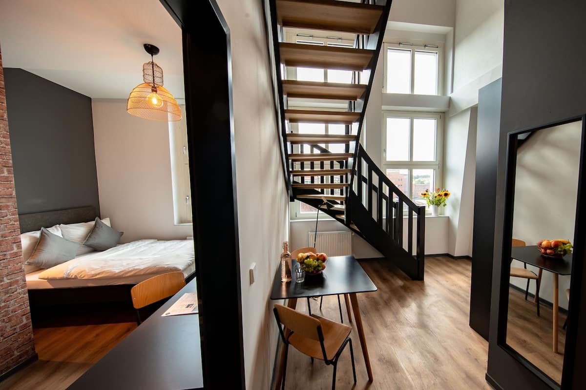 Um apartamento loft moderno com beliche, área de jantar com mesa e cadeiras, escada em espiral e grandes janelas.