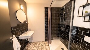 Un baño moderno con un lavabo blanco, un espejo, paredes con azulejos negros y una zona de ducha.