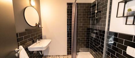 Une salle de bain moderne avec un lavabo blanc, un miroir, des murs recouverts de carreaux noirs et un espace douche.