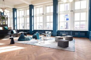 Una habitación amplia con ventanas grandes, piso de madera en espiga y muebles modernos, incluyendo un sofá, sillas y otomanas.
