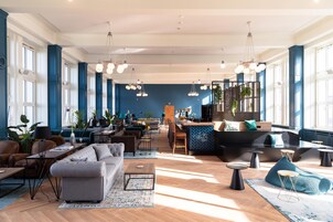 Un amplio vestíbulo de hotel con diversas zonas de estar, un bar y grandes ventanales que dejan entrar luz natural.