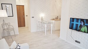 A modern living room with a glass dining table, clear chairs, a white sofa, and a TV mounted on a wall with a perforated design. - Warsaw Concierge Opera Apartment (Warsaw)
