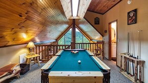 Una mesa de billar en una habitación con techos de madera y vista al exterior.