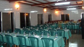 A banquet hall with rows of tables and chairs, large windows, and a high ceiling with wooden beams. - Al Djadid (Domoni)