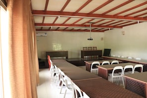 A conference room with long tables and white chairs, wooden beams on the ceiling, and a whiteboard on the wall.