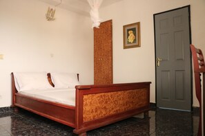 A bedroom with a wooden bed, a door, a framed picture, and a decorative wall hanging. - Al Djadid (Domoni)