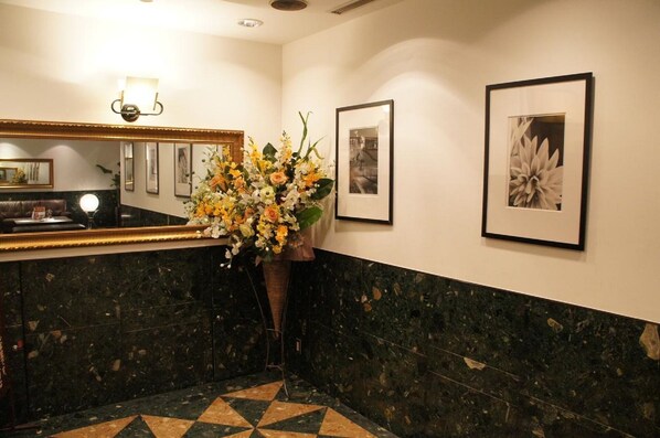 Un hall d’hôtel avec un comptoir d’accueil, un grand miroir, un vase de fleurs et des tableaux encadrés accrochés au mur.