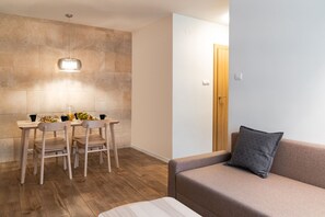 Un salón moderno con una mesa de comedor de madera, dos sillas, un sofá gris con un cojín y una lámpara en la pared.