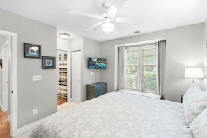 A bedroom with a bed, a ceiling fan, a TV, a window with blinds, and a nightstand.