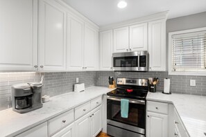 A modern kitchen with white cabinets, a stainless steel microwave, a built-in oven, and a coffee maker.