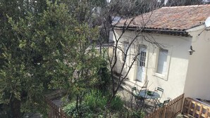 Ein Haus mit einem Ziegeldach, einem eingezäunten Garten und einem kleinen Tisch mit Stühlen.